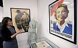 In this Monday, May 21, 2018, photo, Sue Wilkins, director of education at The International Museum of World War II, in Natick, Mass., stands near a 1933 propaganda poster, right, that praised the Nazi organization German Labor Front, which was created after the Nazis eliminated trade unions. (AP Photo/Steven Senne)