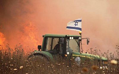 An undated photo of an Israeli farmer in the Gaza-area driving his tractor next to a  field apparently set aflame by a burning kite flown from the Gaza Strip. (Courtesy)