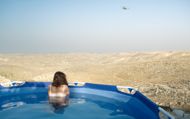 A Tekoa resident sits in a pool overlooking the Judean desert. (Neta Mor/Unsettling)