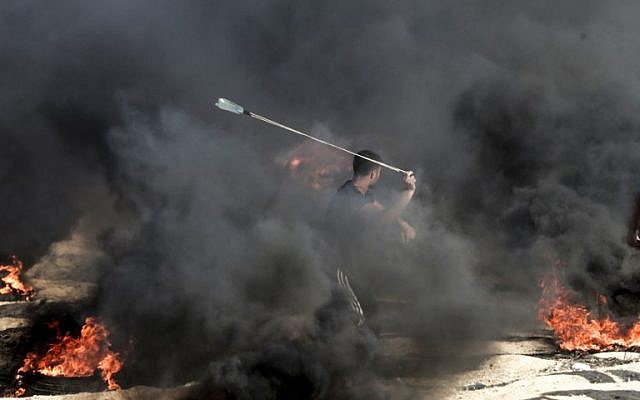A Palestinian protester uses a slingshot to throw a stone towards Israeli forces as smoke billows from burning tires during a demonstration along the border with the Gaza strip east of Gaza city on June 1, 2018. (AFP PHOTO / Mahmud Hams) A Palestinian protester uses a slingshot to throw a stone towards Israeli forces as smoke billows from burning tires during a demonstration along the border with the Gaza strip east of Gaza city on June 1, 2018. (AFP PHOTO / Mahmud Hams)