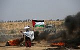 A woman stands holding a Palestinian flag with a cloth sack placed above her head before a barbed-wire fence and next to burning tires, during clashes following a demonstration near the border with Israel east of Khan Yunis in the southern Gaza Strip on June 8, 2018. (AFP/ SAID KHATIB)