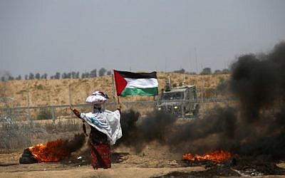 A woman stands holding a Palestinian flag with a cloth sack placed above her head before a barbed-wire fence and next to burning tires, during clashes following a demonstration near the border with Israel east of Khan Yunis in the southern Gaza Strip on June 8, 2018. (AFP/ SAID KHATIB)