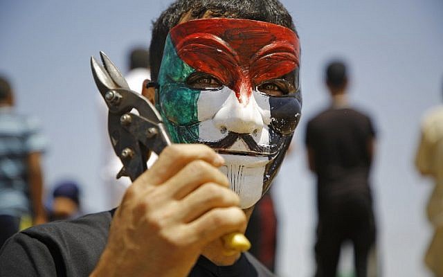 A Palestinian youth wearing a Guy Fawkes mask coloured with the Palestinian flag brandishes a pair of shears during a mass demonstration along the border fence east of Jabalia in the central Gaza Strip on June 8, 2018.(Mohammed Abed/AFP)