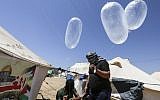 Illustrative. Masked Palestinian men prepare inflated latex condoms loaded with flammable material to be flown toward Israel, at the Israel-Gaza border in al-Bureij, central Gaza Strip on June 14, 2018. (AFP PHOTO / MAHMUD HAMS)