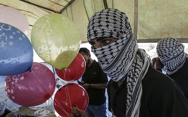 File: Masked Palestinians prepare balloons loaded with flammable material to be flown toward Israel, at the Israel-Gaza border in al-Bureij, central Gaza Strip on June 14, 2018. (AFP/Mahmud Hams) File: Masked Palestinians prepare balloons loaded with flammable material to be flown toward Israel, at the Israel-Gaza border in al-Bureij, central Gaza Strip on June 14, 2018. (AFP/Mahmud Hams)