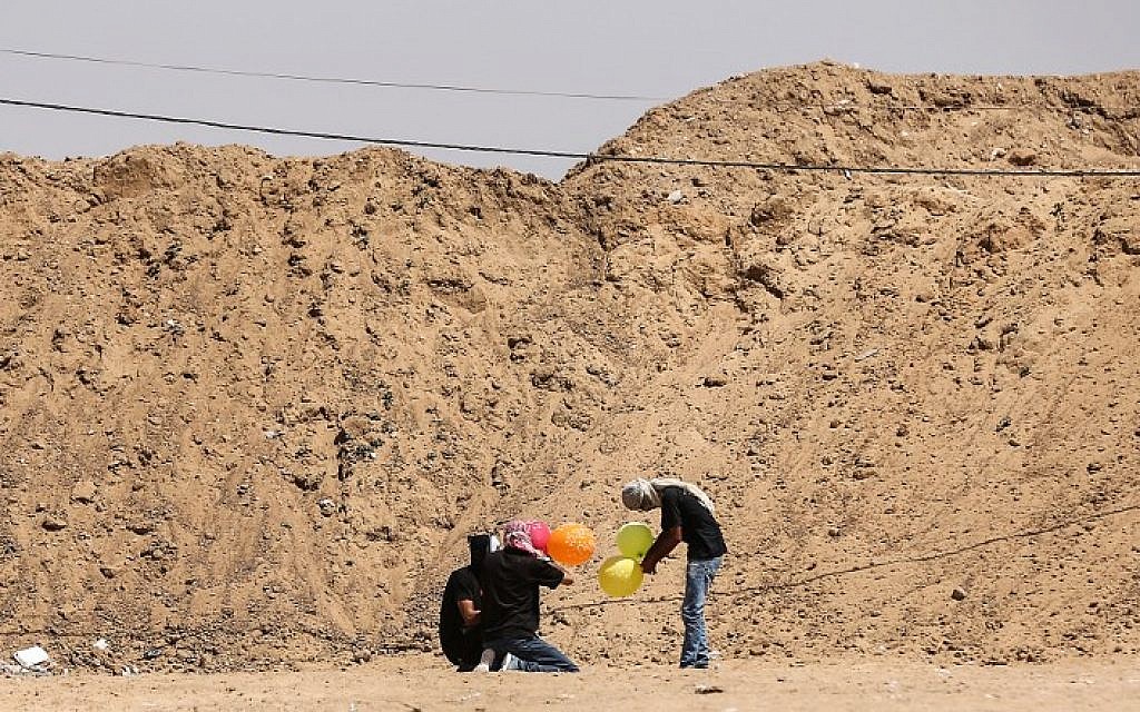 Illustrative: Gazans load balloons with flammable material to be flown toward Israel, at the Israel-Gaza border in al-Bureij, central Gaza Strip on June 14, 2018. (AFP/Mahmud Hams)