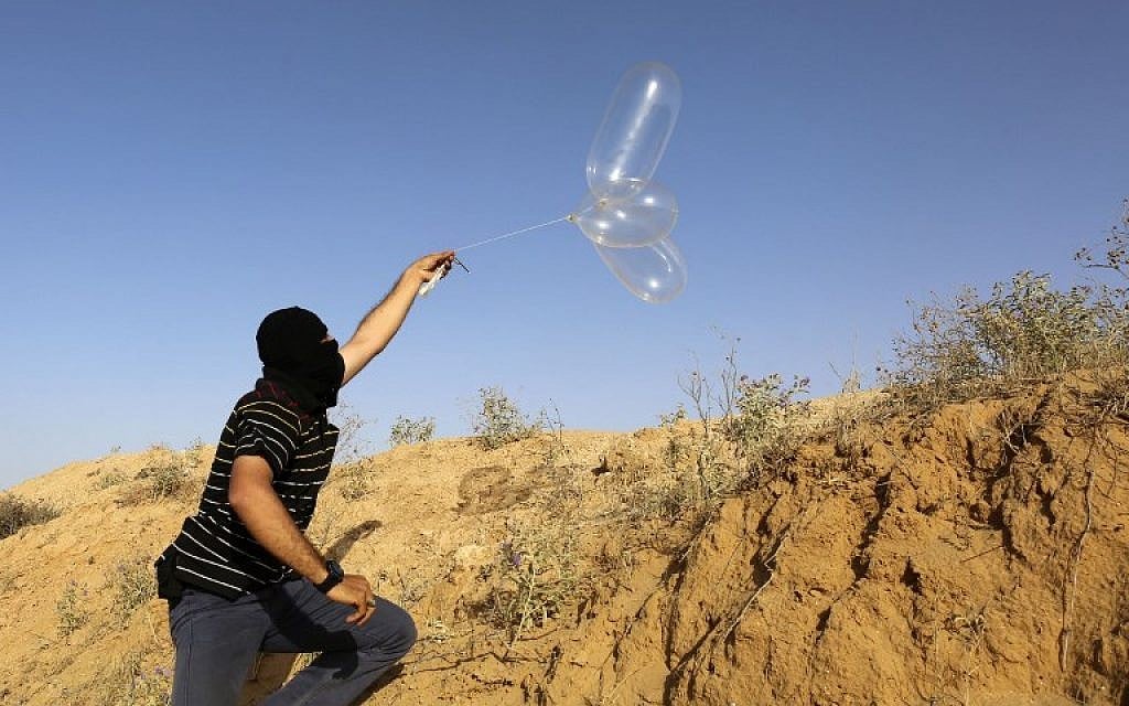 Illustrative: A masked Palestinian man launches a balloon loaded with flammable materials toward Israel from the southern Gaza town of Rafah on June 17, 2018. (AFP Photo/Said Khatib)