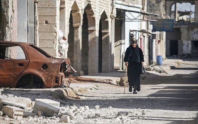 A woman walks with a cane past a destroyed car down a street in Al-Hirak in the eastern Daraa province countryside in southern Syria on June 21, 2018. (AFP PHOTO / Mohamad ABAZEED) A woman walks with a cane past a destroyed car down a street in Al-Hirak in the eastern Daraa province countryside in southern Syria on June 21, 2018. (AFP PHOTO / Mohamad ABAZEED)