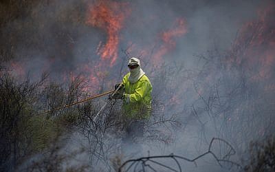 Illustrative. A firefighter extinguishing a fire in a field near the Gaza Strip that was sparked by a flaming object flown from the Palestinian enclave, on June 5, 2018. (Yonatan Sindel/ Flash90)
