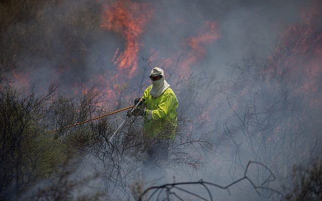 Illustrative. A firefighter extinguishing a fire in a field near the Gaza Strip that was sparked by a flaming object flown from the Palestinian enclave, on June 5, 2018. (Yonatan Sindel/ Flash90) Illustrative. A firefighter extinguishing a fire in a field near the Gaza Strip that was sparked by a flaming object flown from the Palestinian enclave, on June 5, 2018. (Yonatan Sindel/ Flash90)