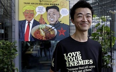 Zach Wen, 34, co-founder of Harmony Nasi Lemak, poses in front of an advertisement  showing cartoon caricatures of US President Donald Trump and North Korean leader Kim Jong Un, supposedly the inspiration behind a local dish, the "Trump-Kim Chi Nasi Lemak," in Singapore, on June 7, 2018. (AP Photo/Wong Maye-E)