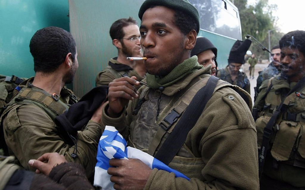 An Israeli soldier holds a national flag as he smokes a cigarette near the Israel-Gaza border after his infantry unit left the Gaza Strip on January 18, 2009. (Menahem Kahana/AFP/Getty Images/via JTA) An Israeli soldier holds a national flag as he smokes a cigarette near the Israel-Gaza border after his infantry unit left the Gaza Strip on January 18, 2009. (Menahem Kahana/AFP/Getty Images/via JTA)