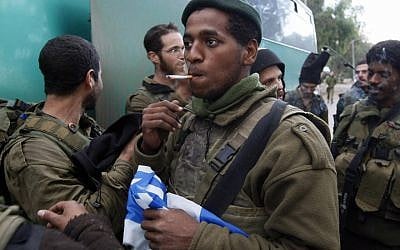 An Israeli soldier holds a national flag as he smokes a cigarette near the Israel-Gaza border after his infantry unit left the Gaza Strip on January 18, 2009. (Menahem Kahana/AFP/Getty Images/via JTA)
