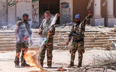 Syrian government soldiers burn an opposition flag while flashing the victory gesture at the Nassib border crossing with Jordan in the southern province of Daraa on July 7, 2018 (AFP PHOTO / Youssef KARWASHAN)