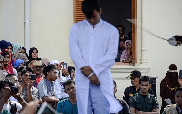 Onlookers watch as a member of Indonesia's Sharia police (R) whips a man (C) accused of having gay sex during a public caning ceremony outside a mosque in Banda Aceh, capital of Aceh province on July 13, 2018. (AFP/CHAIDEER MAHYUDDIN) Onlookers watch as a member of Indonesia's Sharia police (R) whips a man (C) accused of having gay sex during a public caning ceremony outside a mosque in Banda Aceh, capital of Aceh province on July 13, 2018. (AFP/CHAIDEER MAHYUDDIN)