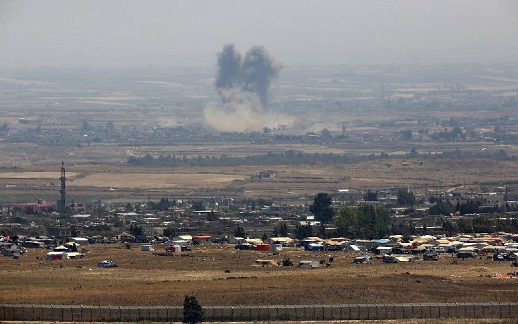 A picture taken on July 18, 2018, from the Israeli Golan Heights shows smoke rising above buildings during unidentified ai strikes across the border fence opposite a camp for displaced Syrians near the village of al-Rafeed in the southern Syrian province of Daraa. (AFP PHOTO / JALAA MAREY)