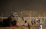 Illustrative: Palestinians throw stones towards Israeli soldiers during a demonstration along the border between Israel and the Gaza Strip, east of Gaza City on July 27, 2018. (AFP Photo/Mahmud Hams)