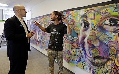 In this June 20, 2018, photo, vice president of marketing and communications for UNICEF USA Francesco De Flaviis, left, talks with co-founder and co-director of Artolution, Max Levi Frieder, of Denver, beside a mural created by Rohingya refugees that's displayed at the offices of UNICEF USA, in New York. (AP Photo/Richard Drew)
