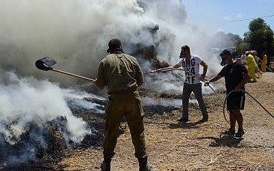Israeli firefighters and security teams fight a fire at and around a cowshed, caused by a kite loaded with an incendiary device from Gaza, at Kibbutz Nahal-Oz on July 21, 2018. (Gili Yaari/FLASH90)