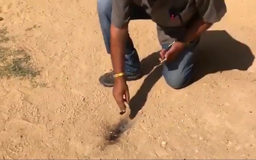 A man inspects where a fire balloon landed in the playground of kindergarten in the Sdot Negev Regional Council on July 17, 2018. (screen capture: Channel 10)