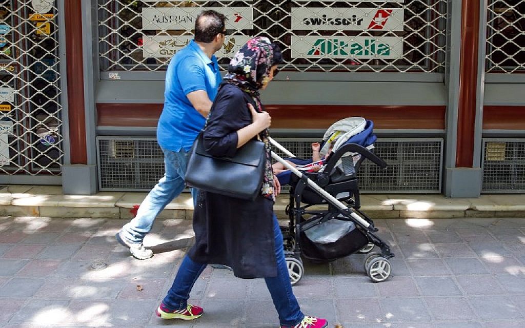 An Iranian family walks past the shuttered window of the closed offices of a travel agency showing the logos of various air lines in the capital Tehran on August 24, 2018. (AFP/ STRINGER)
