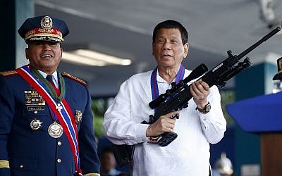 Philippine President Rodrigo Duterte jokes to photographers as he holds an Israeli-made Galil rifle which was presented to him by outgoing Philippine National Police Chief Director General Ronald "Bato" Dela Rosa, left, at the turnover-of-command ceremony on April 19, 2018, at Camp Crame in suburban Quezon city northeast of Manila, Philippines. (AP Photo/Bullit Marquez)