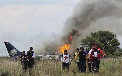 Red Cross workers and rescue workers carry an injured person on a stretcher, right, as airline workers, left, walk away from the site where an Aeromexico airliner crashed in a field near the airport in Durango, Mexico, July 31, 2018 (Red Cross Durango via AP)