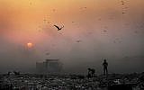 FILE- In this Oct. 17, 2014, file photo, a thick blanket of smoke is seen against the setting sun as young ragpickers search for reusable material at a garbage dump in New Delhi, India (AP Photo/Altaf Qadri, File)
