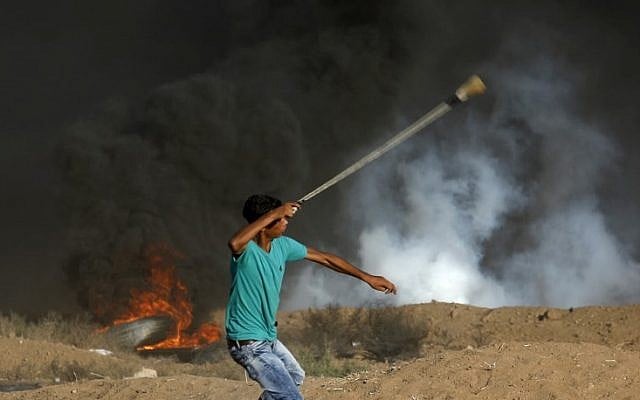 Illustrative: A Palestinian protester uses a slingshot to throw stone toward Israeli forces firing tear gas during a demonstration along the border fence east of Gaza City on September 14, 2018. (AFP/Said Khatib) Illustrative: A Palestinian protester uses a slingshot to throw stone toward Israeli forces firing tear gas during a demonstration along the border fence east of Gaza City on September 14, 2018. (AFP/Said Khatib)