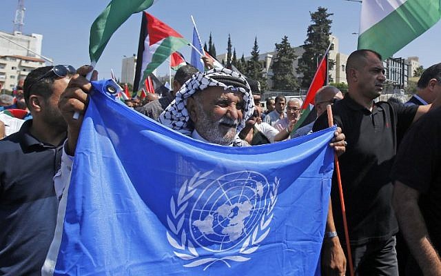 Palestinian protesters wave UN and national flags in front of a fabiricated giant refugee card of their President Mahmud Abbas, during a protest against the US decision earlier this year to cut funds to UN aid to Palestinians, in the West Bank city of Bethlehem, on September 26, 2018. (AFP/Musa Al SHAER) Palestinian protesters wave UN and national flags in front of a fabiricated giant refugee card of their President Mahmud Abbas, during a protest against the US decision earlier this year to cut funds to UN aid to Palestinians, in the West Bank city of Bethlehem, on September 26, 2018. (AFP/Musa Al SHAER)