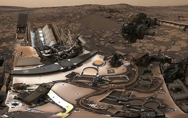 This composite image from Aug. 9, 2018 photos made available by NASA shows the Curiosity rover at Vera Rubin Ridge on Mars. A thin layer of dust is visible on the nuclear-powered rover, the result of a storm that enveloped the planet this summer. The darkish sky is from dust still in the atmosphere. (NASA/JPL-Caltech/MSSS via AP) This composite image from Aug. 9, 2018 photos made available by NASA shows the Curiosity rover at Vera Rubin Ridge on Mars. A thin layer of dust is visible on the nuclear-powered rover, the result of a storm that enveloped the planet this summer. The darkish sky is from dust still in the atmosphere. (NASA/JPL-Caltech/MSSS via AP)