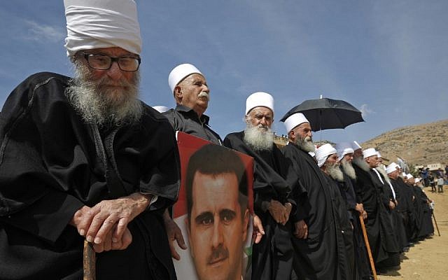 Elderly members of the Druze community stand holding a portrait of Syrian President Bashar al-Assad during a rally in the Druze village of Majdal Shams in the Israeli-annexed Golan Heights on October 6, 2018 commemorating the 45th anniversary of the 1973 Arab-Israeli war. / AFP PHOTO / JALAA MAREY