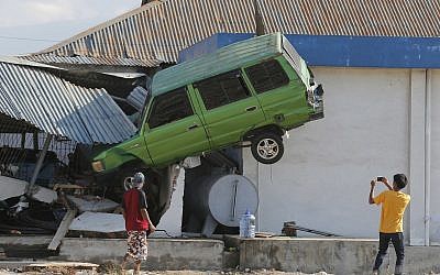 A man takes a photo of a car lifted into the air with his mobile phone following a massive earthquake and tsunami at Talise beach in Palu, Central Sulawesi, Indonesia, Oct. 1, 2018 (AP Photo/Tatan Syuflana)