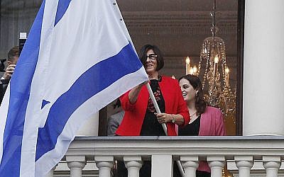 Israeli Ambassador Anna Azari holds the Israeli flag from a balcony of the historic Bristol Hotel in Warsaw, Poland, during a ceremony on Tuesday, Oct. 23, 2018. The flag hanging was a re-enactment ceremony marking the 70th anniversary of Israel's first diplomatic outpost as a new nation at the same spot. (AP Photo/Czarek Sokolowski)