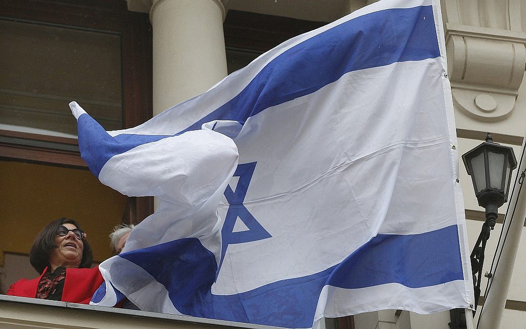 Israeli Ambassador Anna Azari holds the Israeli flag from a balcony of the historic Bristol Hotel in Warsaw, Poland, during a ceremony on Tuesday, Oct. 23, 2018.  (AP/Czarek Sokolowski)