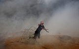 Illustrative. A protester falls down on barbed fence as he runs for cover from tear gas fired by Israeli troops while others burn tires near the Gaza Strip's border with Israel during a protest east of Khan Younis, southern Gaza Strip, Friday, Oct. 5, 2018 (AP Photo/Adel Hana)