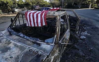 An American flag is draped over the charred remains of an old pickup truck entering Point Dume along the pacific coast highway in Malibu, California, on November 11, 2018. (AP Photo/Richard Vogel)