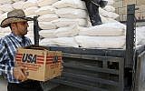 A Palestinian carries a box of vegetable oil as he walks past bags of flour on a truck donated by USAID, or the United States Agency for International Development, at a depot in the West Bank village of Anin near Jenin, June 4, 2008 (AP Photo/Mohammed Ballas)