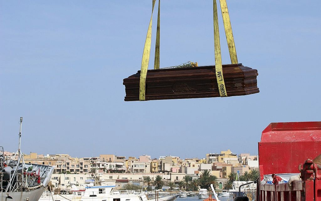 In this October 12, 2013 file photo, the casket of one of the migrants who died when their boat capsized off in the Canal of Sicily is lifted by crane to an Italian Navy ship at the Lampedusa island harbor. (AP Photo/Mauro Buccarello)