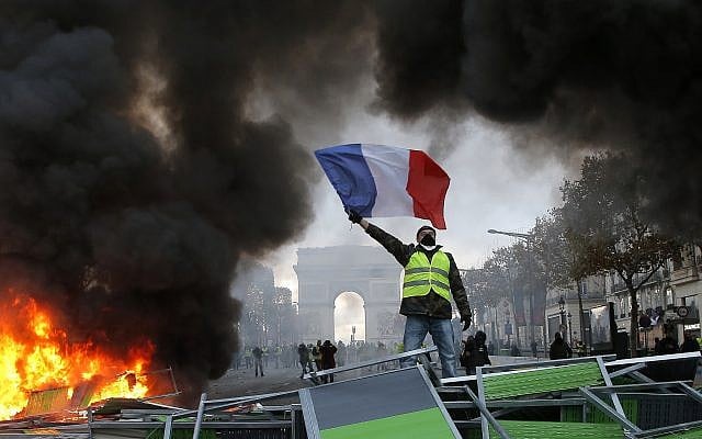 A demonstrator waves the French flag onto a burning barricade on the Champs-Elysees avenue with the Arc de Triomphe in background, during a demonstration against the rising of the fuel taxes, Saturday, Nov. 24, 2018 in Paris. (AP/Michel Euler) A demonstrator waves the French flag onto a burning barricade on the Champs-Elysees avenue with the Arc de Triomphe in background, during a demonstration against the rising of the fuel taxes, Saturday, Nov. 24, 2018 in Paris. (AP/Michel Euler)