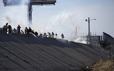 Migrants in Mexico stand amid tear gas launched by US agents at the border with the US, right of fence, after a group of migrants pushed past Mexican police at the Chaparral crossing in Tijuana, Mexico, Nov. 25, 2018 (AP Photo/Ramon Espinosa)