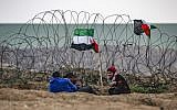 Palestinian youths sit next to a Palestinian flag by the barbed-wire fence along the border with Israel east of Gaza City during a border demonstration on December 7, 2018. (Said Khatib/AFP)