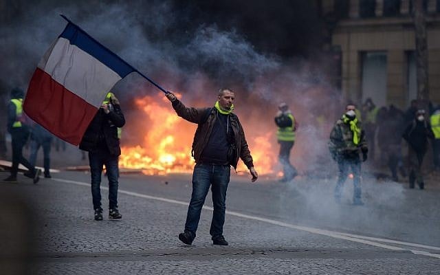 A "yellow vest" protestor waves a French flag during clashes with riot police amid tear gas near the Champs Elysees in Paris on December 8, 2018. (Lucas Barioulet/AFP)