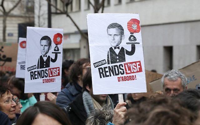 Protesters hold placards showing a portrait of French President Emmanuel Macron and reading "give back the ISF first" during a march on December 8, 2018 in Paris. The ISF is a solidarity tax on wealth that Macron shrank last year to cover only real estate, a move seen by protesters as a tax break for the rich. (Jacques Demarthon/AFP)