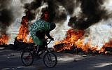 A Palestinian wears a flag with Koranic inscriptions as he rides his bicycle in front of burning tires  near the Hawara checkpoint south of the West Bank city of Nablus on December 14, 2018. (Photo by JAAFAR ASHTIYEH / AFP)