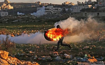 A Palestinian uses a slingshot to hurl stones amid smoke during clashes with Israeli troops in Ramallah on December 14, 2018. (Abbas Momani/AFP)