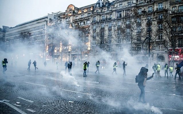 Protesters wearing yellow vests stand amid tear gas during a demonstration against rising costs of living they blame on high taxes on the Champs-Elysees avenue in Paris, on December 15, 2018 (Abdul ABEISSA / AFP) Protesters wearing yellow vests stand amid tear gas during a demonstration against rising costs of living they blame on high taxes on the Champs-Elysees avenue in Paris, on December 15, 2018 (Abdul ABEISSA / AFP)
