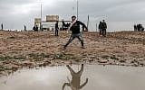 A Palestinian stands next to a rain puddle as he uses a slingshot to hurl an object during clashes with Israeli troops along the border, east of Gaza city, on December 28, 2018. (Mahmud Hams/AFP)