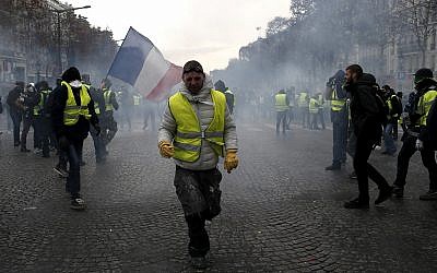 A demonstrator wearing a yellow vest grimaces through tear gas, Dec. 8, 2018 in Paris (AP Photo/Rafael Yaghobzadeh)