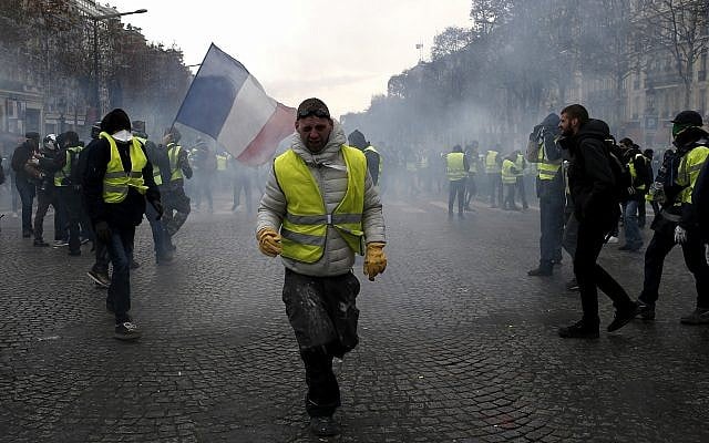 A demonstrator wearing a yellow vest grimaces through tear gas, Dec. 8, 2018 in Paris (AP Photo/Rafael Yaghobzadeh)